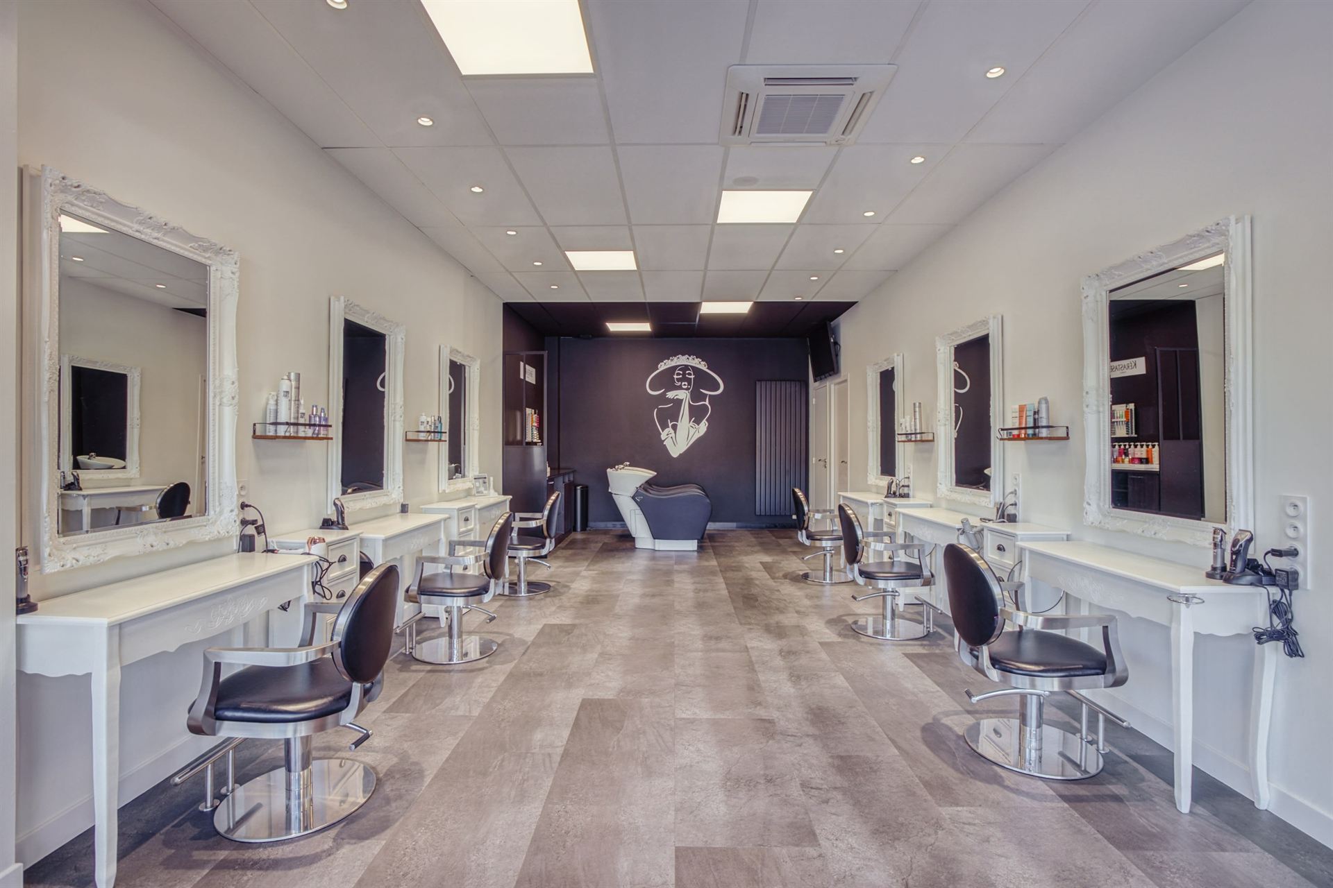 Intérieur du salon Arti's Coiffure à Châteaubourg : miroirs baroques blancs et fauteuils noirs
